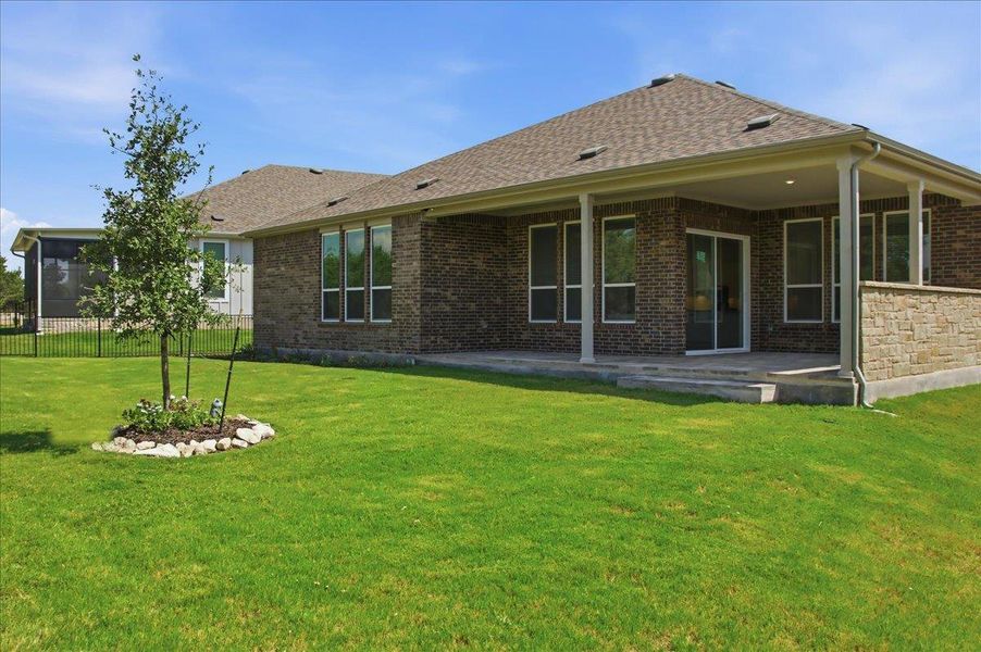 A neatly manicured lawn extends from a spacious brick home featuring a covered patio and ample windows. A neatly manicured lawn extends from a spacious brick home featuring a covered patio and ample windows.