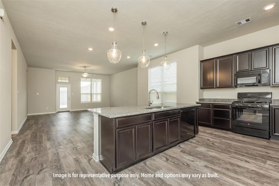 Kitchen with black appliances, light stone countertops, an island with sink, dark wood finish cabinetry, and hanging light fixtures