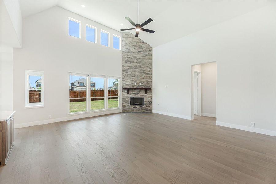 Open living room with vaulted ceiling, stone fireplace, hardwood floors, and large windows Open living room with vaulted ceiling, stone fireplace, hardwood floors, and large windows