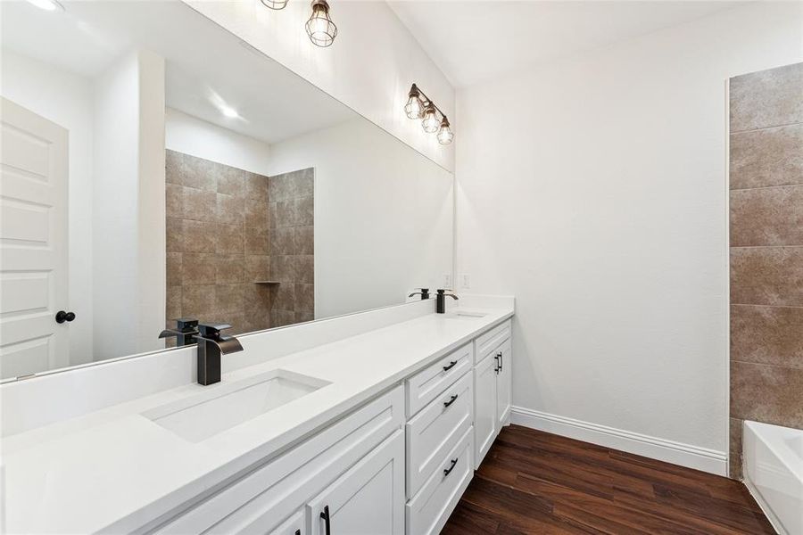 Bathroom with dark wood finished floors, double vanity, and bathing tub / shower combination