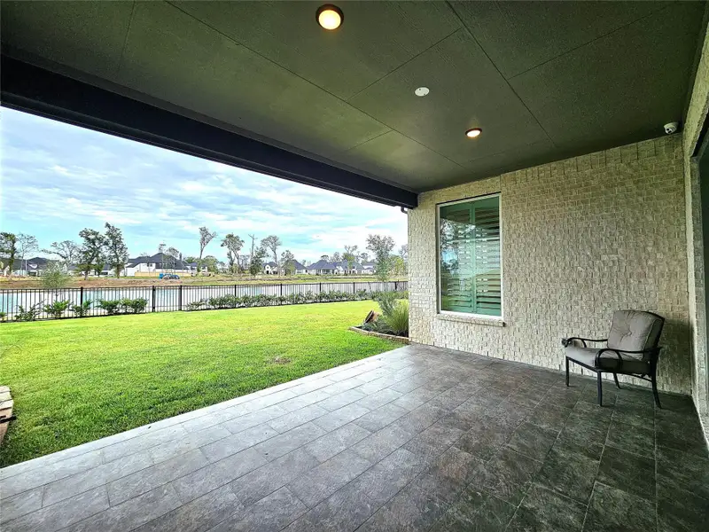 This photo showcases a covered patio with a tiled floor, overlooking a well-maintained lawn and a scenic water view. The space is ideal for relaxing or entertaining, with ample room for outdoor furniture.
