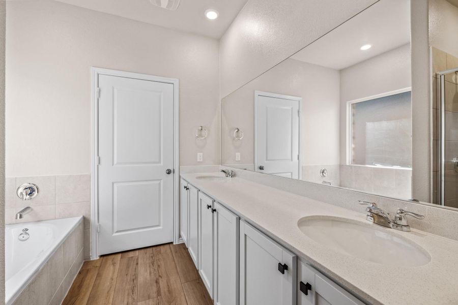 Bathroom featuring a garden tub, double vanity, light wood-style flooring, and a shower stall