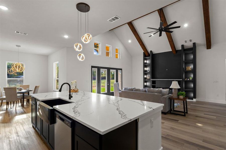Kitchen featuring dark cabinetry, pendant lighting, high vaulted ceiling, light wood-type flooring, and open floor plan