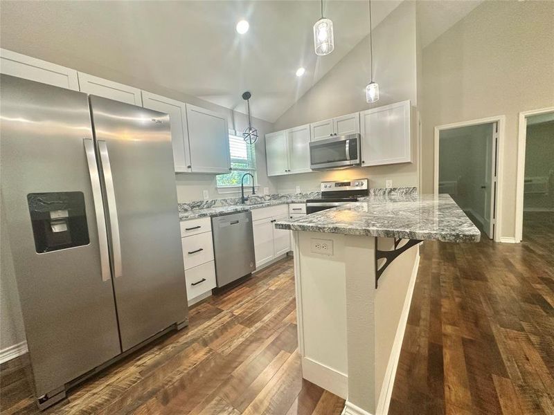 Upstairs Kitchen with appliances with stainless steel finishes, a peninsula, vaulted ceiling, LVP floors, and white cabinetry Upstairs Kitchen with appliances with stainless steel finishes, a peninsula, vaulted ceiling, LVP floors, and white cabinetry