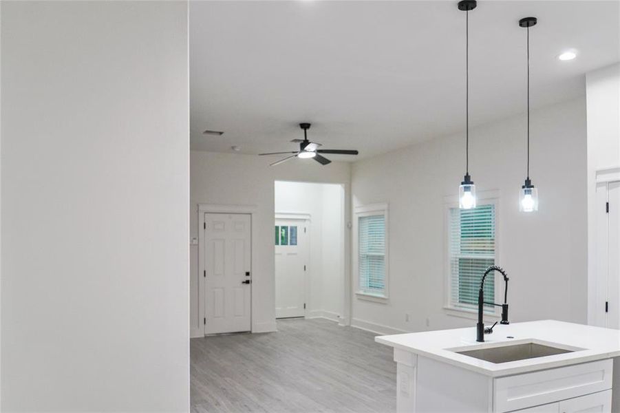 Kitchen with light wood-type flooring, white cabinets, light countertops, decorative light fixtures, and ceiling fan Kitchen with light wood-type flooring, white cabinets, light countertops, decorative light fixtures, and ceiling fan