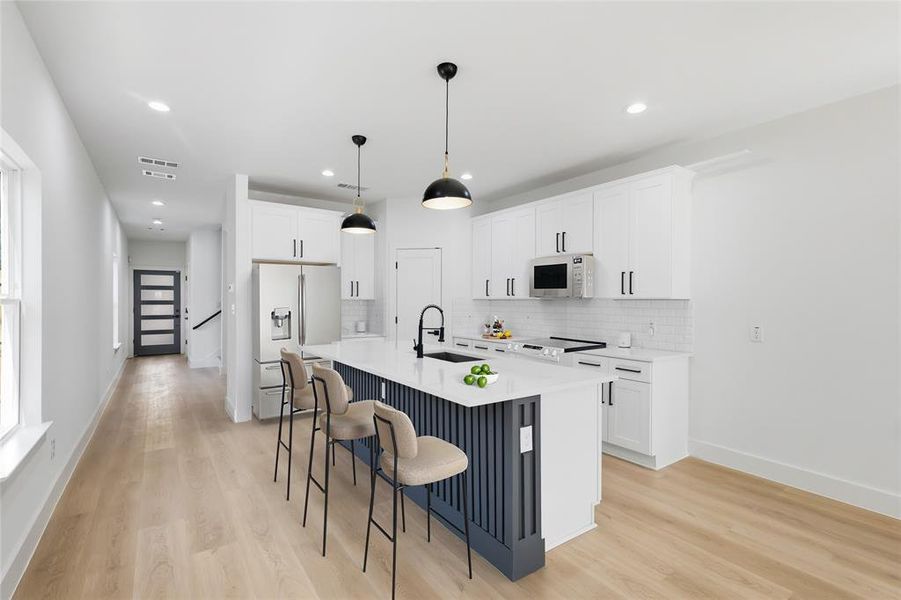 Kitchen with a kitchen breakfast bar, white cabinetry, stainless steel fridge, light wood finished floors, and a kitchen island with sink