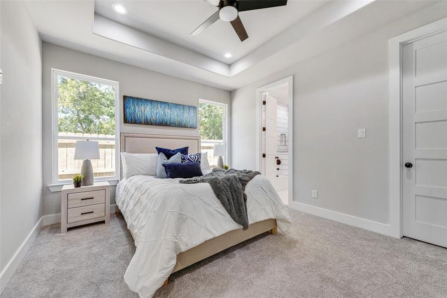 Bedroom featuring a tray ceiling, ceiling fan, light colored carpet, and multiple windows