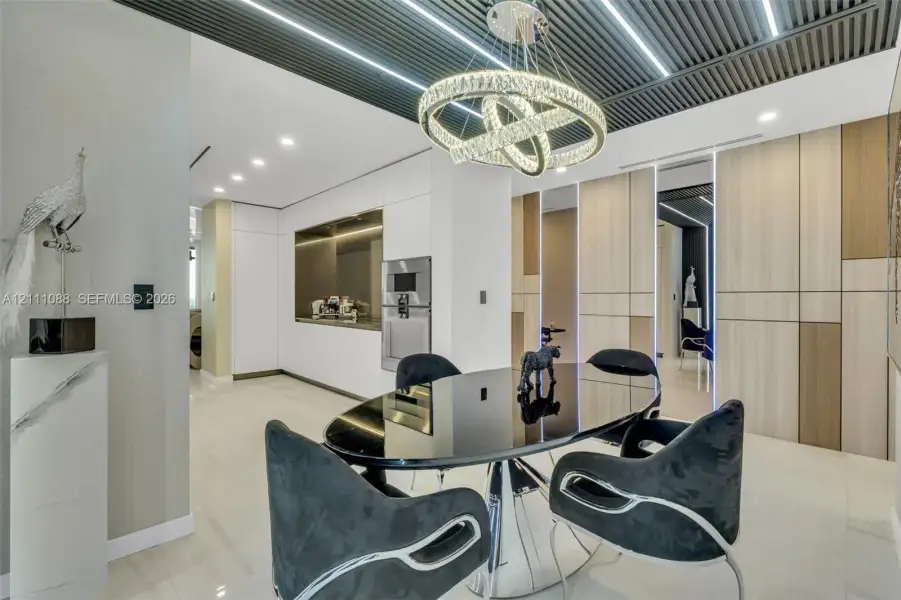Slatted ceiling with integrated linear lighting, custom circular crystal chandelier, built-in floor-to-ceiling cabinetry with wood-finish paneling, and smooth-surface flooring Slatted ceiling with integrated linear lighting, custom circular crystal chandelier, built-in floor-to-ceiling cabinetry with wood-finish paneling, and smooth-surface flooring