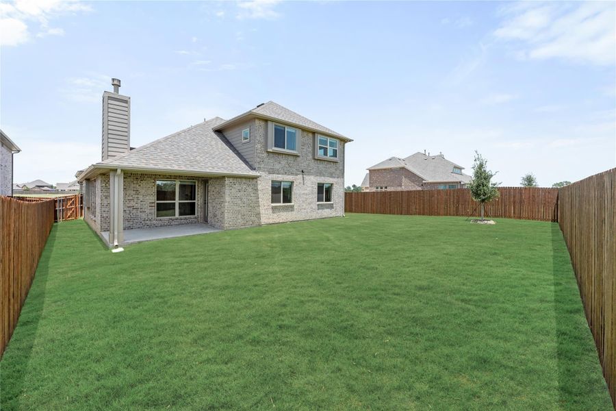 Two-story brick home with covered patio, large grassy backyard, and wood privacy fence