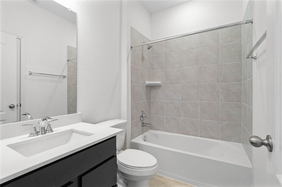 Secondary bathroom features stained cabinets, neutral paint, shower/tub combo with tile surround, large mirror, tile floors, and sleek fixtures and modern finishes.