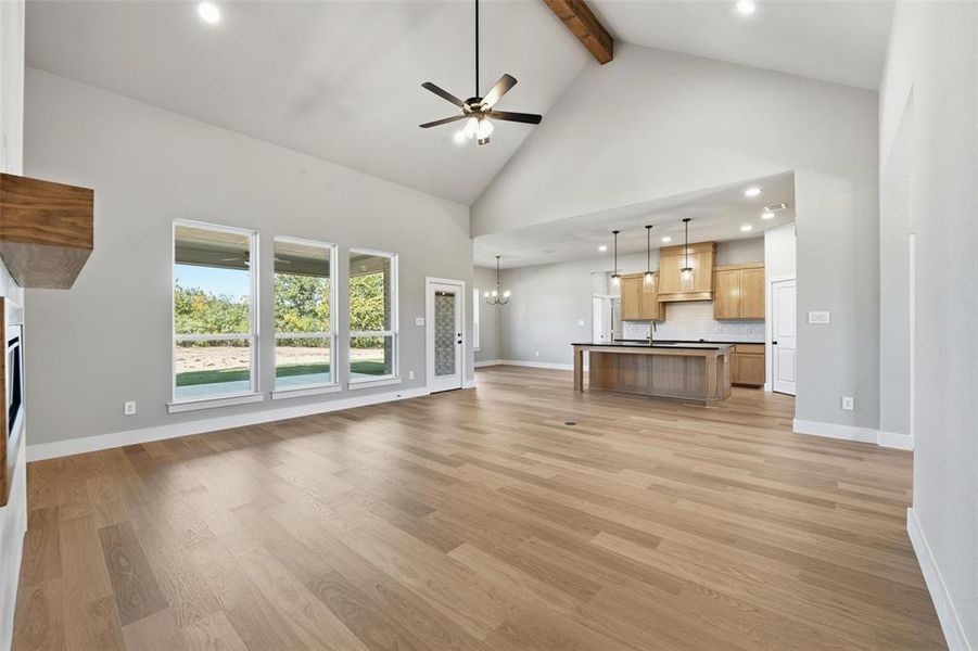 Unfurnished living room with high vaulted ceiling, a ceiling fan, a chandelier, recessed lighting, and beamed ceiling
