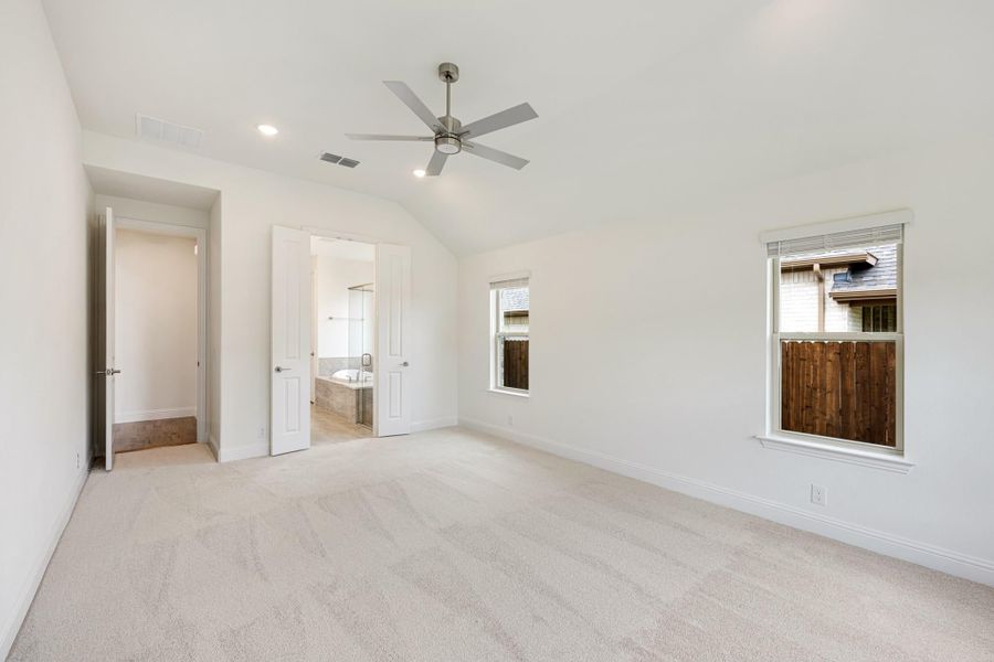 Empty bedroom with vaulted ceiling, ceiling fan, carpet flooring, and open door to ensuite bathroom Empty bedroom with vaulted ceiling, ceiling fan, carpet flooring, and open door to ensuite bathroom