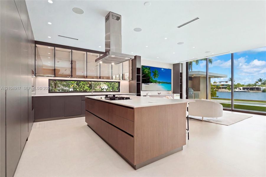 Modern kitchen featuring a large central island, integrated cooktop, stainless steel range hood, and floor-to-ceiling windows