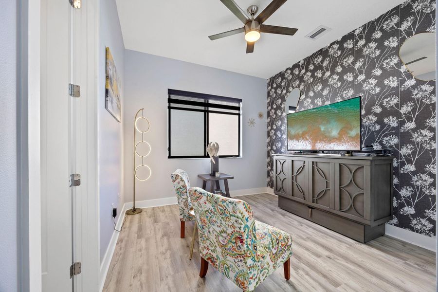 Office area with wood finished floors, an accent wall, wallpapered walls, and a ceiling fan