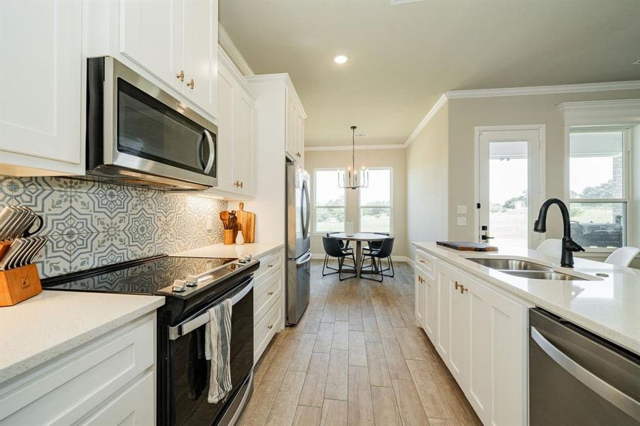 Kitchen featuring stainless steel appliances, light stone counters, tasteful backsplash, white cabinetry, and ornamental molding Kitchen featuring stainless steel appliances, light stone counters, tasteful backsplash, white cabinetry, and ornamental molding