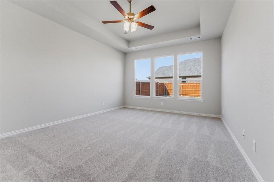 Spare room featuring light colored carpet, a ceiling fan, and a tray ceiling