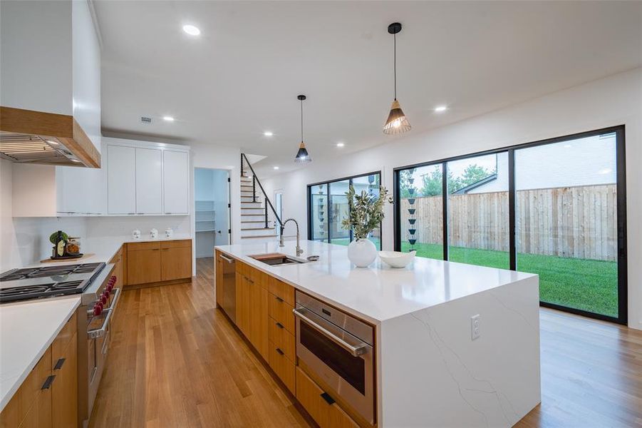 Kitchen featuring wall chimney exhaust hood, a kitchen island with sink, sink, white cabinets, and appliances with stainless steel finishes