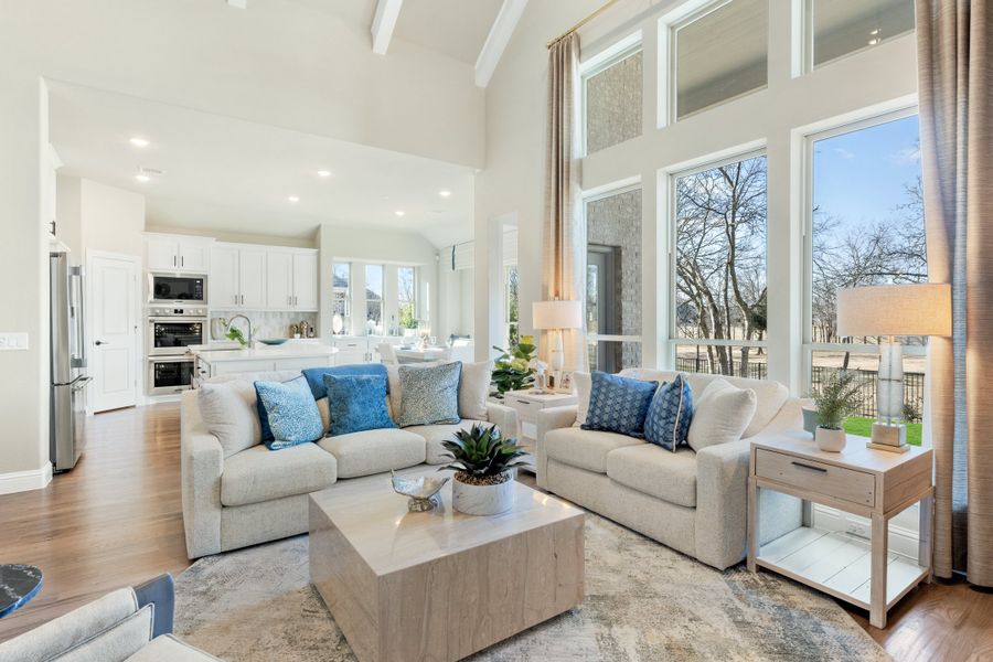 Open-concept living room with vaulted ceiling, two sofas, and large windows overlooking kitchen area Open-concept living room with vaulted ceiling, two sofas, and large windows overlooking kitchen area