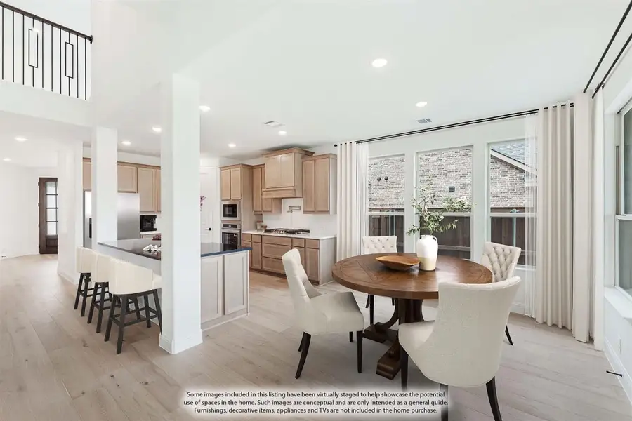Open dining area with round wood table next to kitchen featuring light wood cabinets and high ceilings