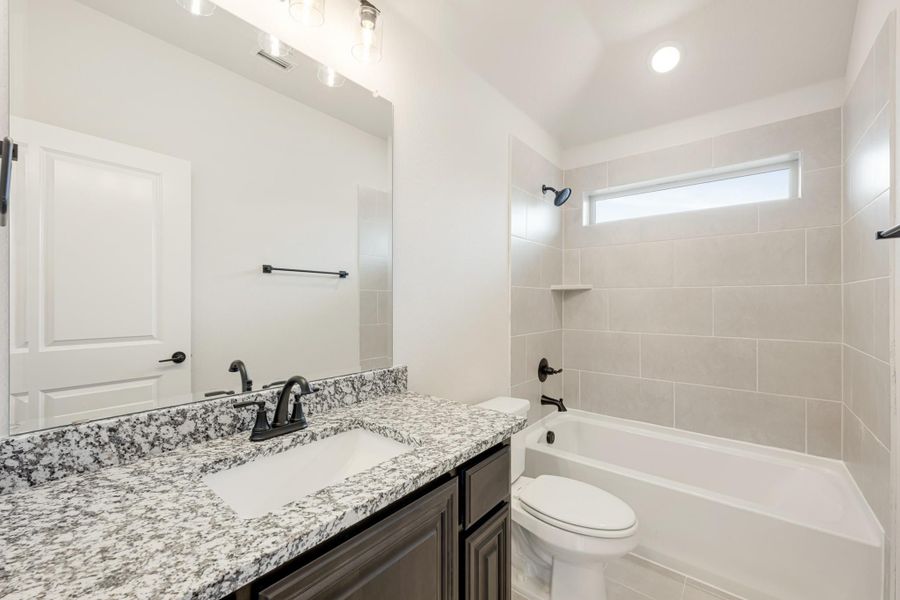Bathroom with granite countertop vanity, tiled shower-tub combo, and dark hardware fixtures