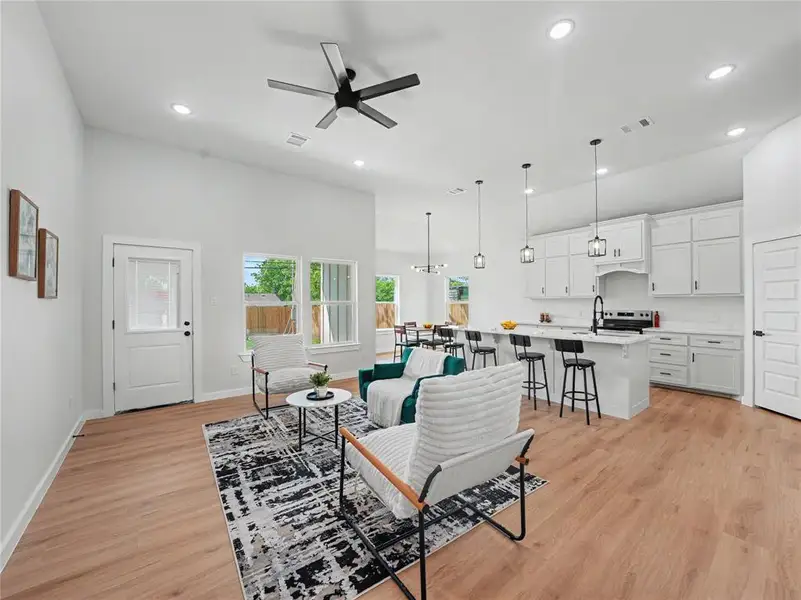 Living area featuring ceiling fan, light wood-style floors, a high ceiling, and hanging lights