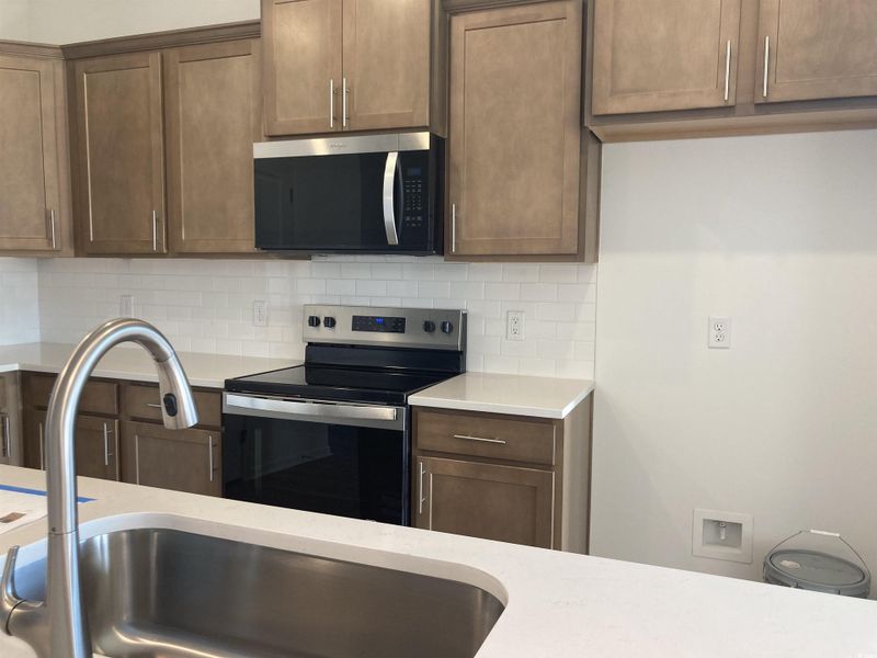 Kitchen with stainless steel appliances, tasteful backsplash, light stone counters, and brown cabinetry
