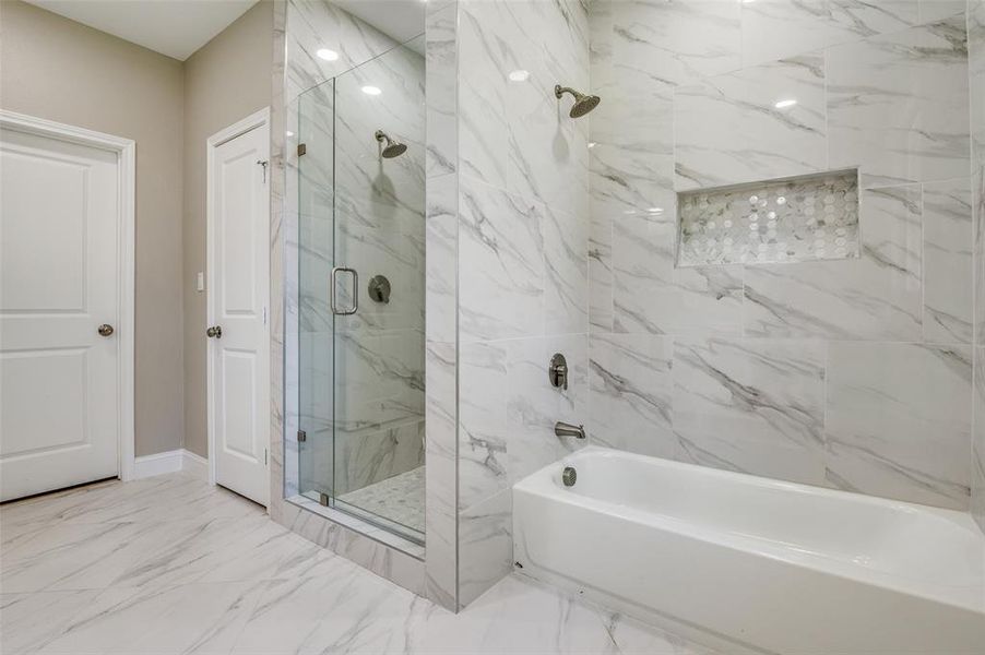 Bathroom featuring a marble finish shower, marble look tiles, and a tub