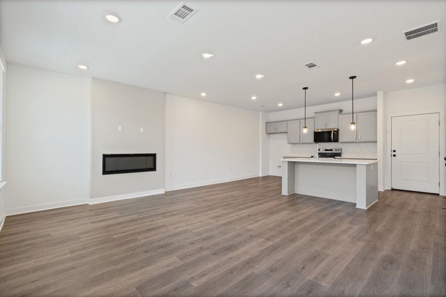 Recessed lighting throughout, wood-finish flooring, built-in linear fireplace, kitchen island with pendant lighting, and light gray cabinetry