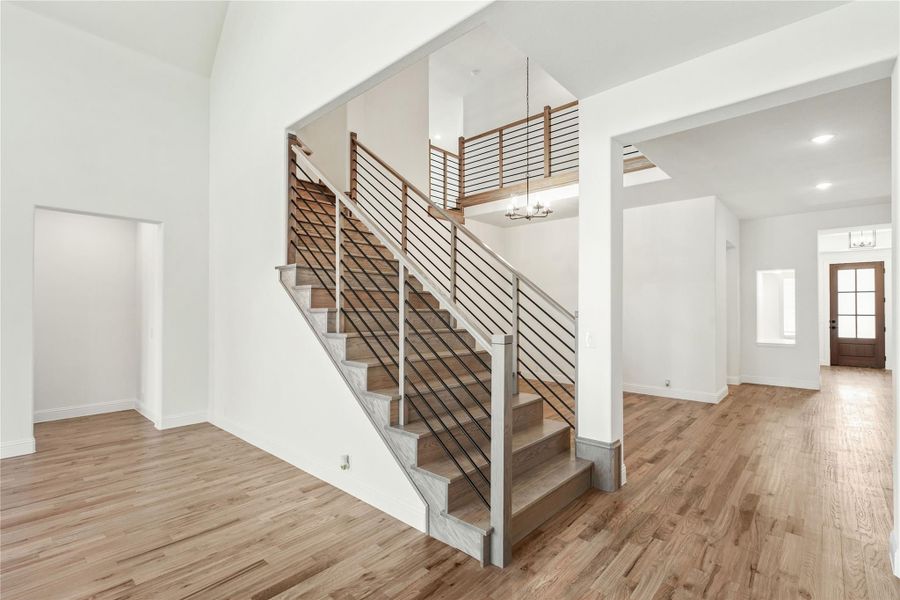 Open foyer with wood staircase, metal rod railing, hardwood floors, and chandelier overhead