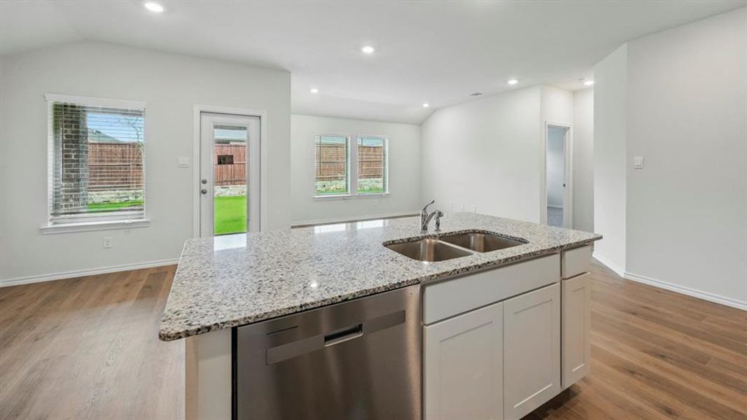 Kitchen island featuring a dual basin sink, stainless steel dishwasher, and a light-toned countertop