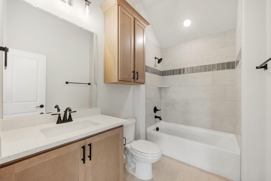 Bathroom with wood vanity, quartz countertop, tiled tub-shower combo, and black fixtures