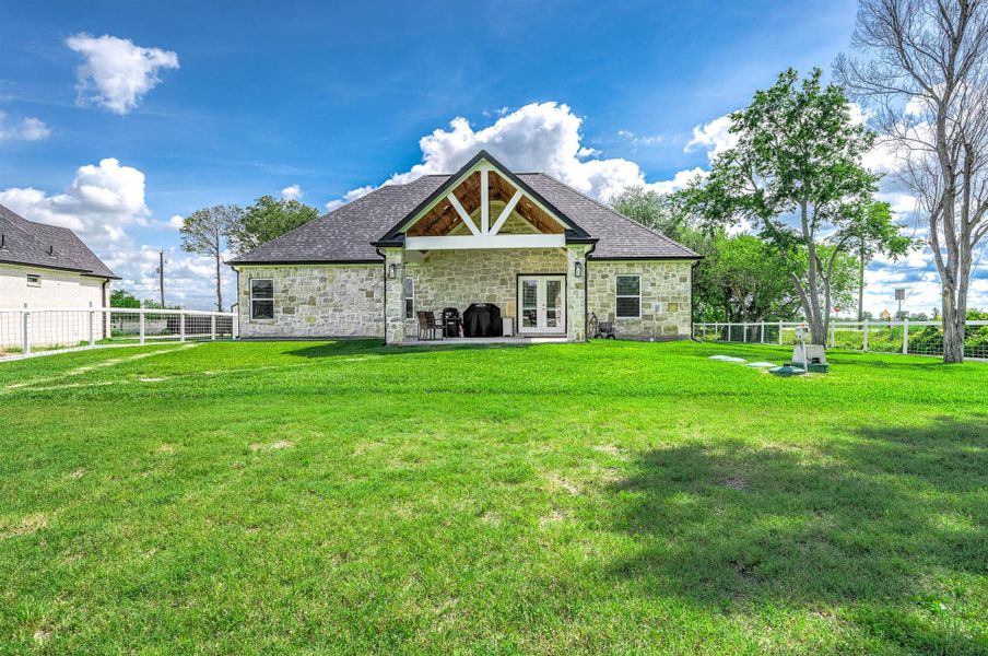 Charming stone home with a spacious backyard, covered patio, and expansive green lawn, creating the perfect setting for outdoor entertaining, relaxing, and everyday enjoyment.