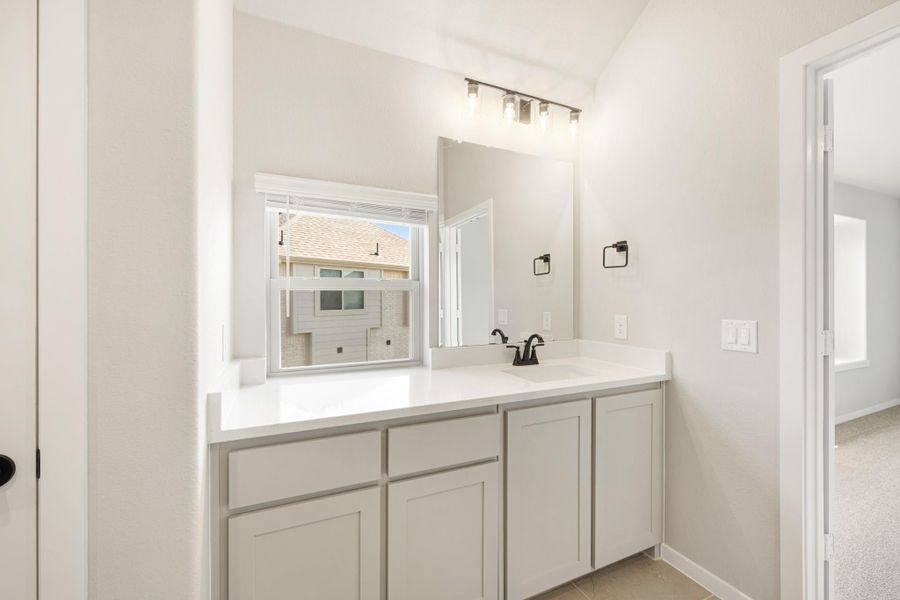 Bathroom vanity with white quartz countertop, gray cabinets, large mirror, and black fixtures above a window.