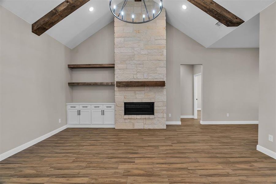 Unfurnished living room with beam ceiling, wood finished floors, a stone fireplace, and high vaulted ceiling Unfurnished living room with beam ceiling, wood finished floors, a stone fireplace, and high vaulted ceiling