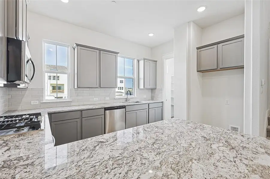 Kitchen with light stone counters, gray cabinetry, appliances with stainless steel finishes, recessed lighting, and decorative backsplash
