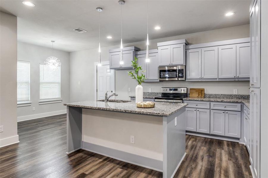 Kitchen with a center island with sink, stainless steel appliances, recessed lighting, light stone countertops, and dark wood-style floors