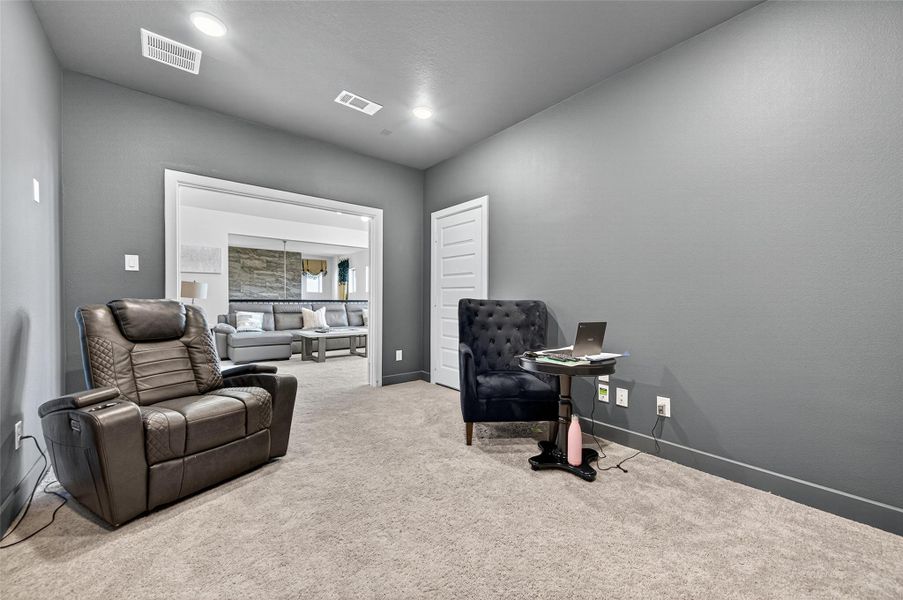 This room serves as a versatile space with plush carpet, neutral gray walls, and recessed lighting. It's furnished with a comfortable leather recliner and a stylish armchair, perfect for a cozy office or reading nook. Double doors open to a living area, enhancing the sense of space. This room serves as a versatile space with plush carpet, neutral gray walls, and recessed lighting. It's furnished with a comfortable leather recliner and a stylish armchair, perfect for a cozy office or reading nook. Double doors open to a living area, enhancing the sense of space.
