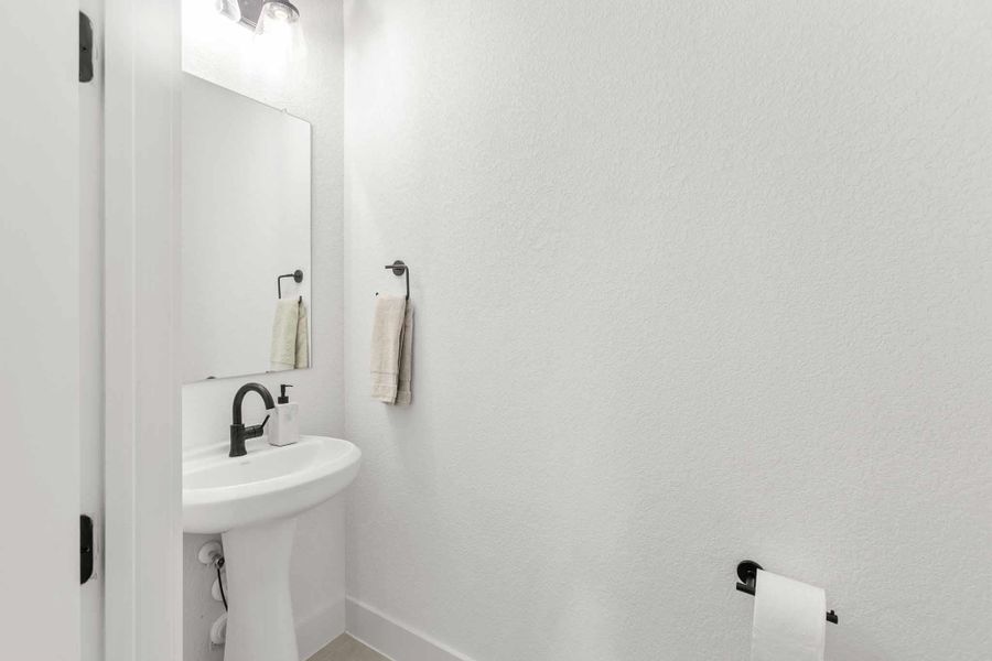 Pedestal sink with black matte faucet, wall-mounted mirror, and overhead vanity lighting