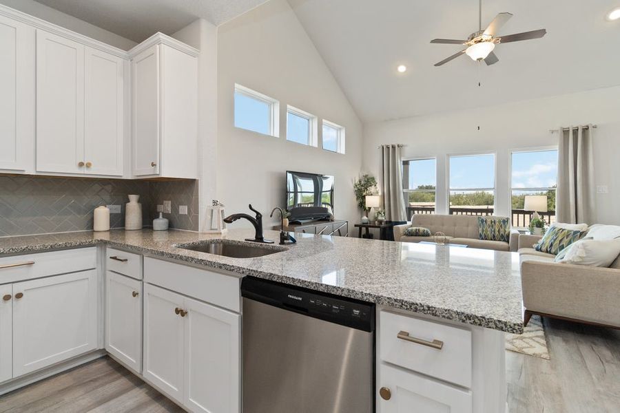 Open-concept kitchen and living room with white cabinets, granite countertops, and vaulted ceiling Open-concept kitchen and living room with white cabinets, granite countertops, and vaulted ceiling