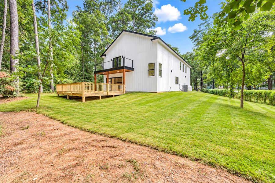 Modern white home with a spacious wooden deck, nestled in a lush, tree-lined yard offering ample outdoor space.