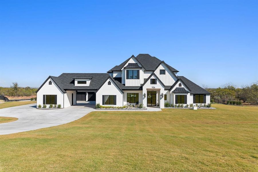 Modern farmhouse style home with a shingled roof, a front yard, board and batten siding, and concrete driveway Modern farmhouse style home with a shingled roof, a front yard, board and batten siding, and concrete driveway