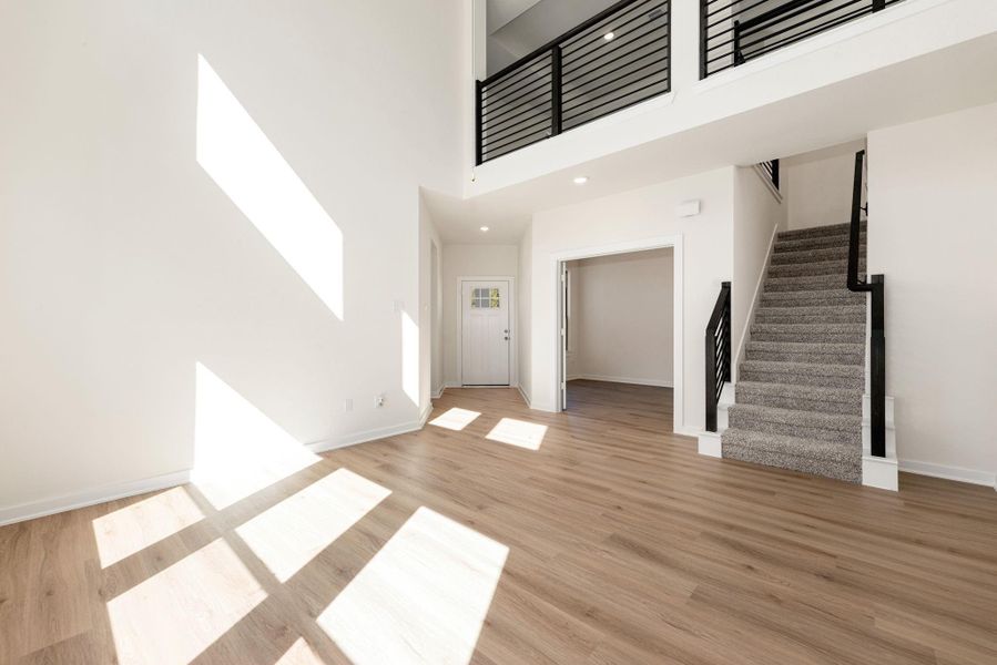 This commanding view from the living area captures the essence of the home's open-concept design and seamless flow. The soaring ceilings, continuous wide-plank flooring, view into the home office, and the grand staircase leading to the upstairs living space. This commanding view from the living area captures the essence of the home's open-concept design and seamless flow. The soaring ceilings, continuous wide-plank flooring, view into the home office, and the grand staircase leading to the upstairs living space.