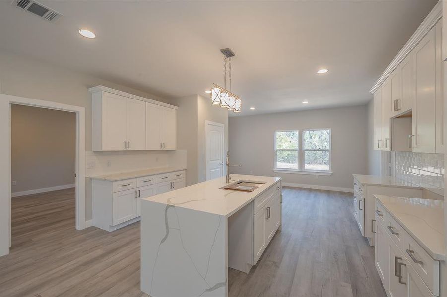 Kitchen with backsplash, a center island with sink, light stone countertops, light wood finished floors, and white cabinetry