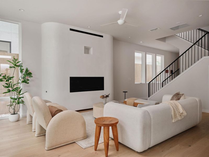 Spacious living area featuring light wood-finish flooring, a contemporary fireplace with a sleek linear firebox, and a modern ceiling fan