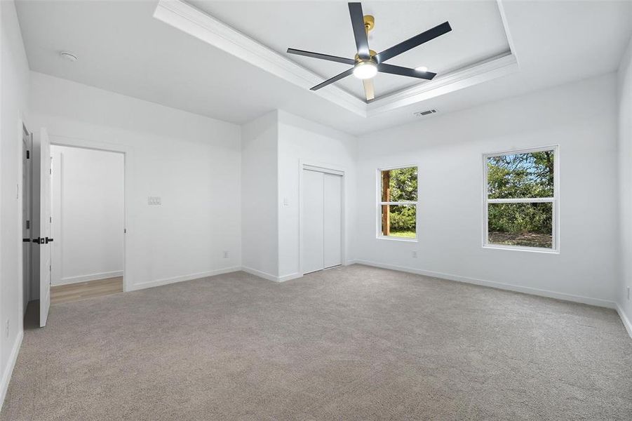 Unfurnished bedroom featuring a tray ceiling, light carpet, a ceiling fan, a closet, and crown molding Unfurnished bedroom featuring a tray ceiling, light carpet, a ceiling fan, a closet, and crown molding