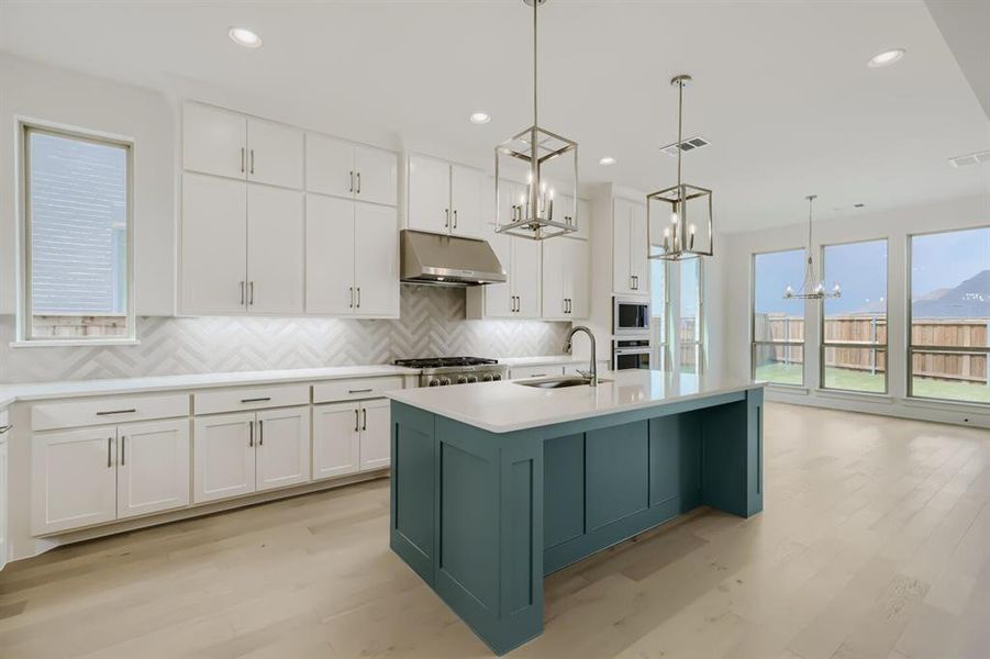 Modern kitchen featuring an expansive center island with a light-toned countertop and teal-painted cabinetry Modern kitchen featuring an expansive center island with a light-toned countertop and teal-painted cabinetry