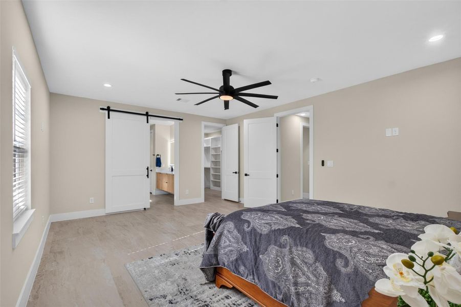 Spacious bedroom featuring a modern ceiling fan, ample natural light, and a stylish sliding barn door leading to the ensuite bathroom and walk-in closet.