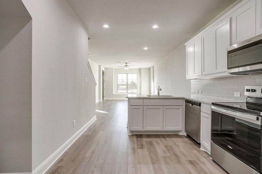 Kitchen with stainless steel appliances, white cabinetry, a peninsula, backsplash, and light wood-style flooring Kitchen with stainless steel appliances, white cabinetry, a peninsula, backsplash, and light wood-style flooring