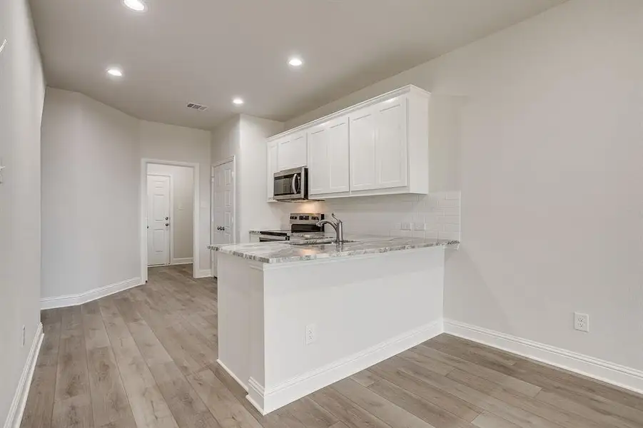 Kitchen with light stone countertops, a peninsula, stainless steel appliances, white cabinets, and light wood finished floors