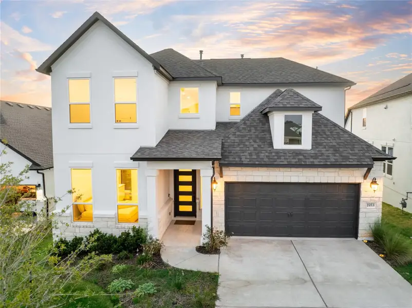 View of front of home featuring a shingled roof, stone siding, a garage, and driveway